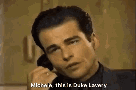 a man in a suit is talking on a cell phone and says michele this is duke lavery
