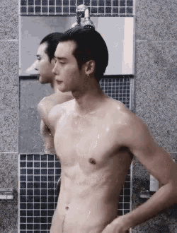 a shirtless man is taking a shower in a bathroom and looking at himself in the mirror .