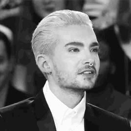a man with white hair and a nose ring is wearing a black suit and white shirt .