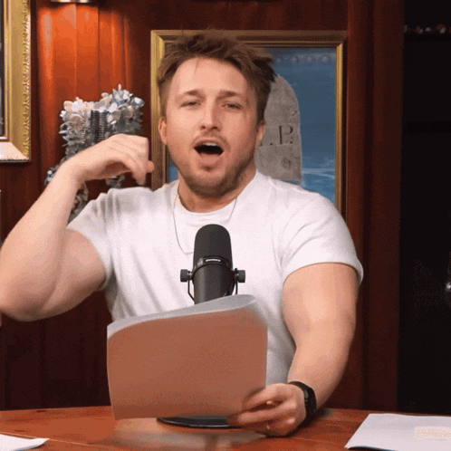 a man sitting in front of a microphone holding a piece of paper