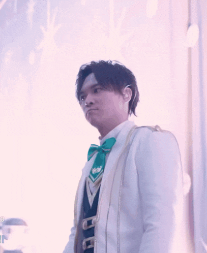 a man in a white suit with a green bow tie looks to the side