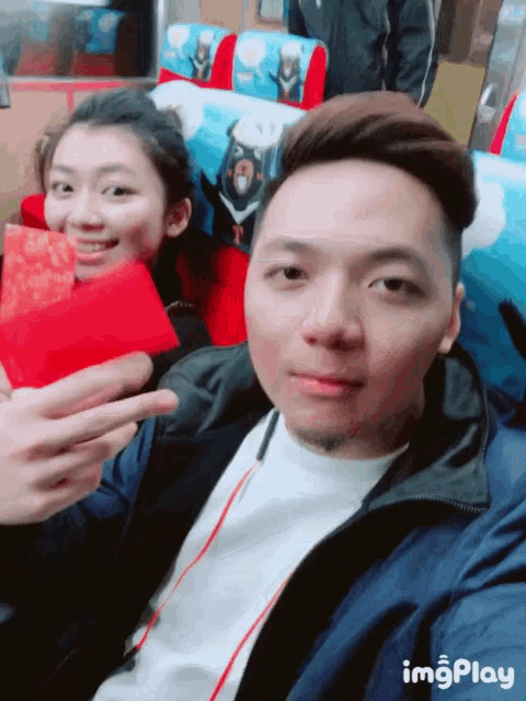 a man and a woman are sitting next to each other and the man is holding a red envelope and the woman is smiling