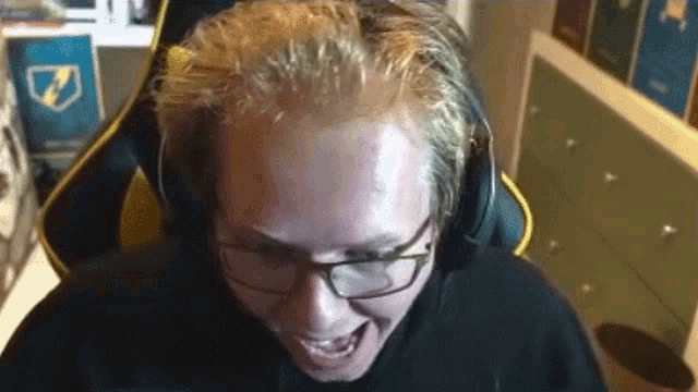 a man wearing glasses and headphones is sitting in a gaming chair and making a funny face .
