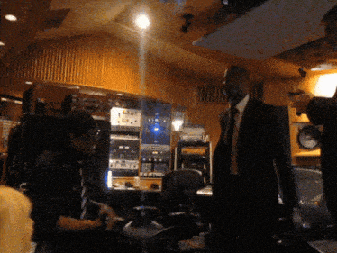 a man in a suit and tie stands in a room with lots of equipment