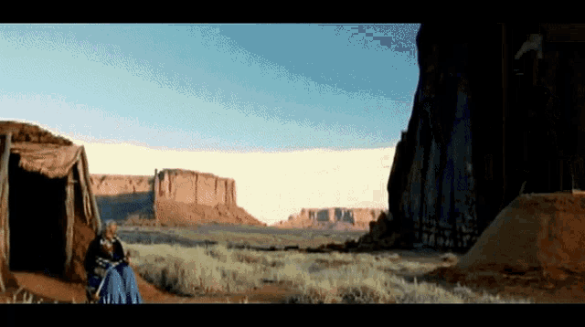 a man sits in front of a tent in a desert landscape