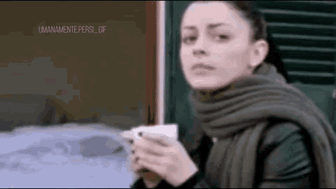 a woman in a scarf is holding a cup of coffee and looking out a window .