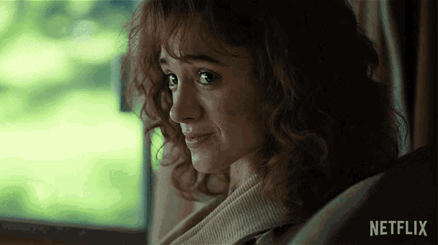 a woman with curly hair is sitting in front of a window with a netflix logo in the corner
