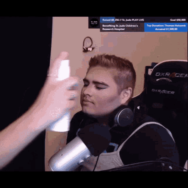 a person spraying something on another person 's face while wearing headphones and a dxracer gaming chair