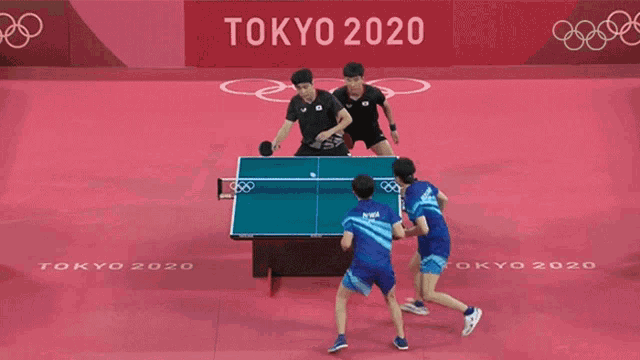 two men are playing ping pong in front of a tokyo 2020 sign