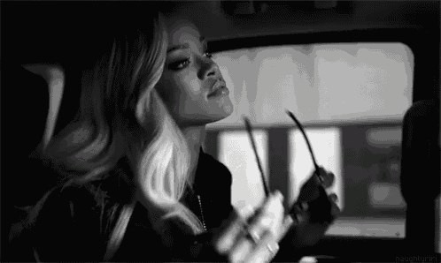 a black and white photo of a woman in a car holding sunglasses .