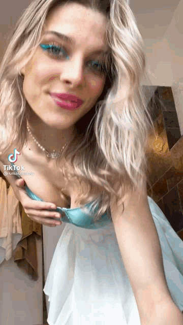a woman wearing a blue bra and a white skirt is taking off her bra .