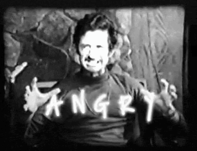 a man wearing a shirt that says `` angry '' is making a funny face in a black and white photo .