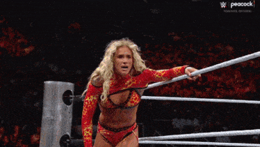 a woman in a fire outfit is in a wrestling ring with a peacock logo behind her