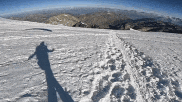 a person 's shadow is cast on a snowy surface