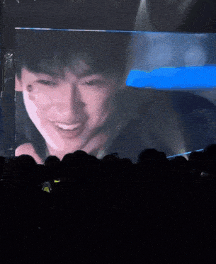 a man is smiling in front of a large screen in a dark room