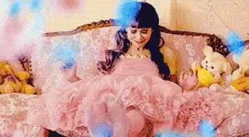 a woman in a pink dress is sitting on a couch surrounded by teddy bears .