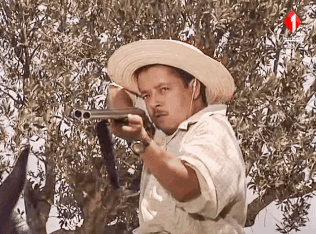 a man in a straw hat holds a shotgun in front of an olive tree