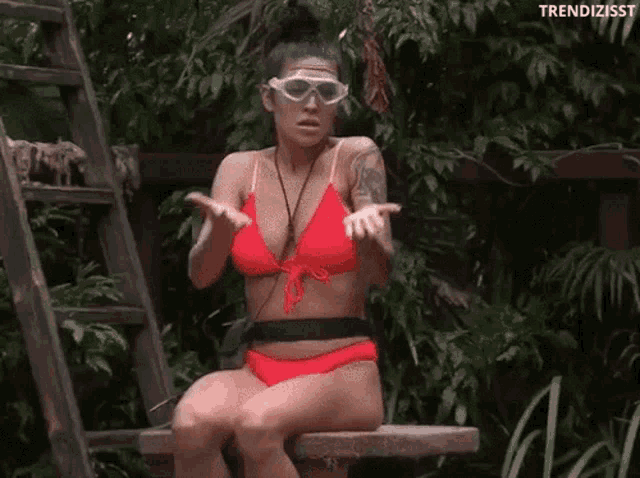 a woman in a red bikini and goggles is sitting on a bench in the jungle .