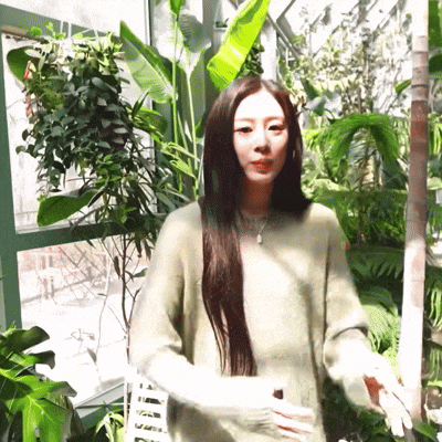 a woman in a green sweater is standing in front of plants