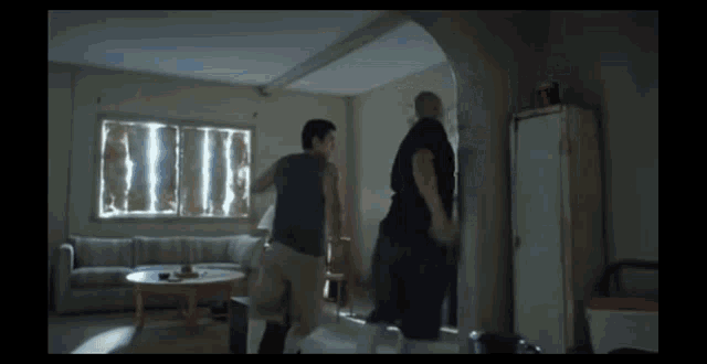 two men are fighting in a living room with a couch and table