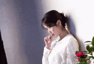 a woman in a white lace top is leaning against a wall with her hand on her chin