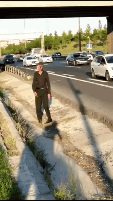 a man walking down a sidewalk next to a highway with cars driving by
