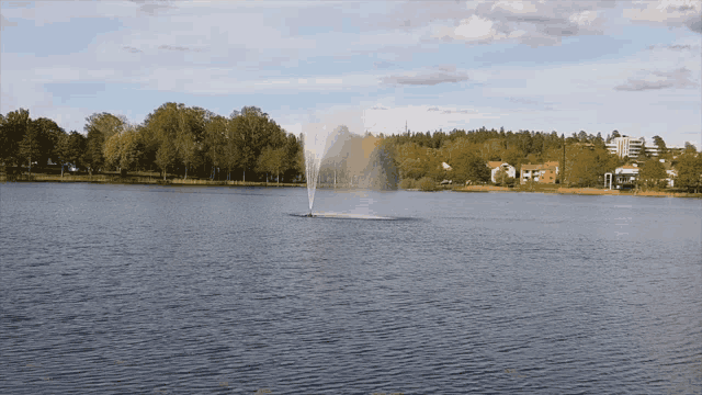 a fountain in the middle of a lake with houses in the background