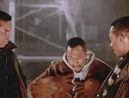 three men are standing next to each other in a dark room and one of them is holding a bag .