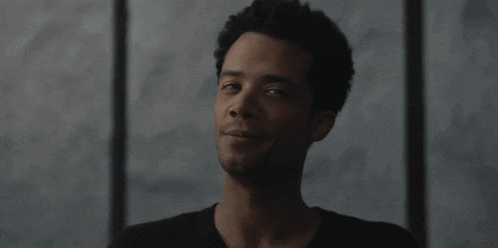 a man in a black shirt is smiling in front of a window