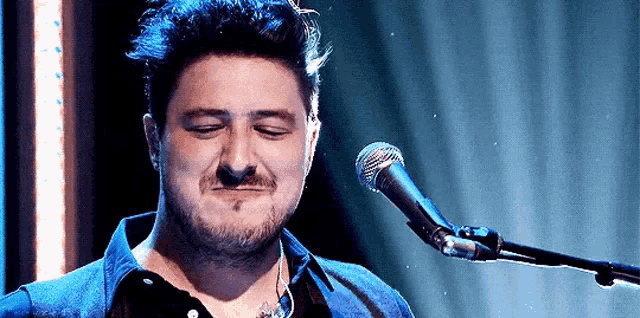 a man with a beard is singing into a microphone with his eyes closed .