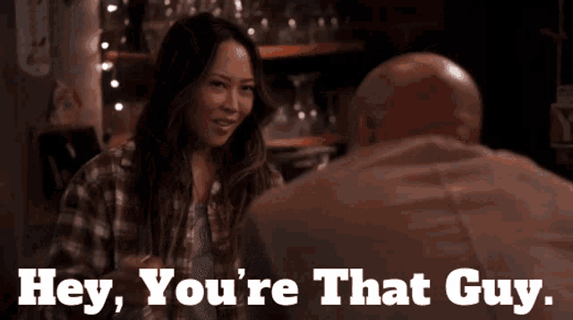 a woman is talking to a bald man with the words hey you 're that guy