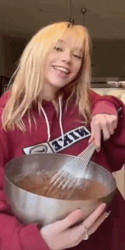 a woman in a red hoodie is holding a bowl of chocolate batter and a whisk .