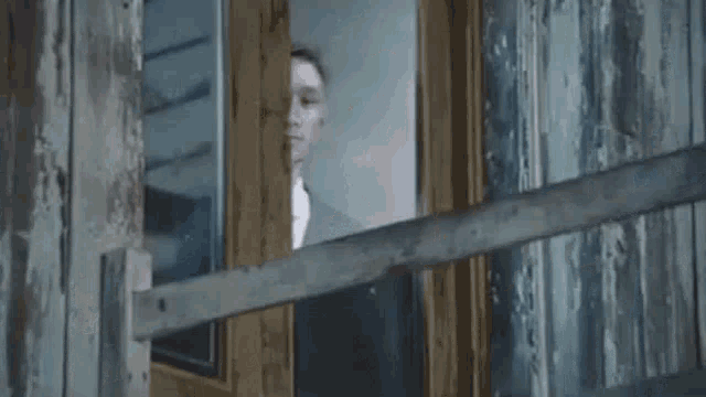a man in a suit and bow tie is looking out of a doorway .