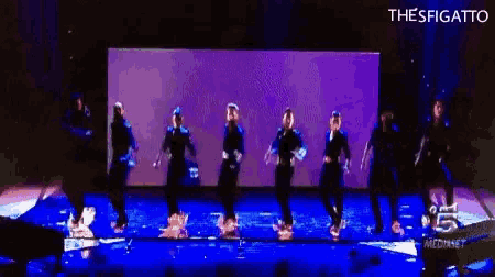 a group of people are dancing on a stage and the word thesfigato is on the bottom right
