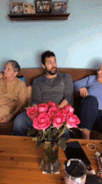 a man sitting on a couch with a vase of pink roses on a table