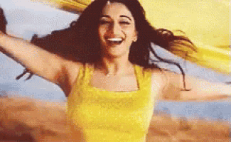 a woman in a yellow tank top is laughing with her arms outstretched and her hair blowing in the wind .