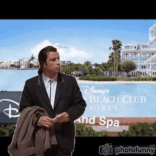 a man in a suit is standing in front of a sign for disney 's beach club resorts