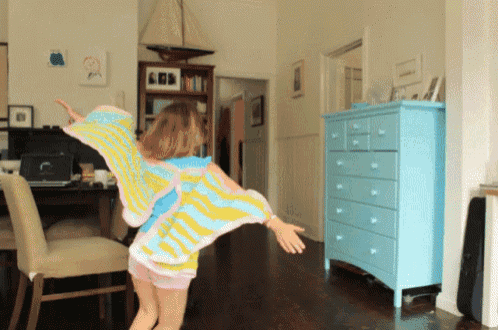 a little girl in a butterfly costume is dancing in a room with a blue dresser