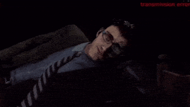 a man with glasses and a tie is laying down in a dark room with transmission error written on the screen