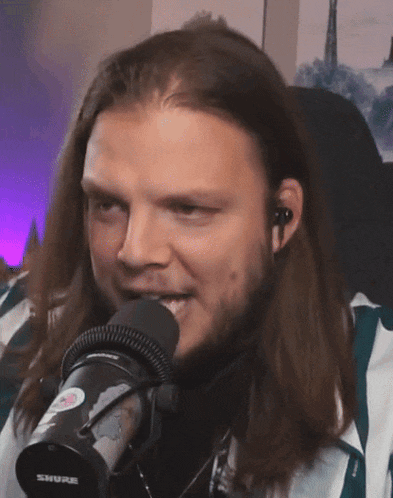 a man with long hair is sitting in front of a shure brand microphone