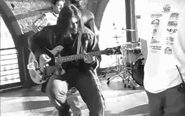 a man is playing a guitar in a black and white photo while standing next to a drum set .