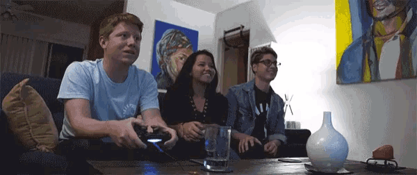 three people are playing a video game in a living room with a vase on the table
