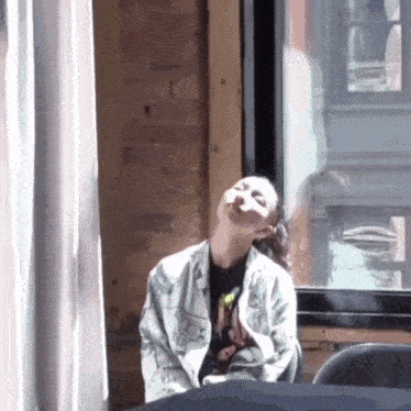 a woman is sitting in front of a window with her head in the air