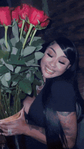 a woman in a black shirt is holding a vase of red roses