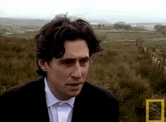 a man in a suit is standing in a field with a national geographic logo on the bottom right