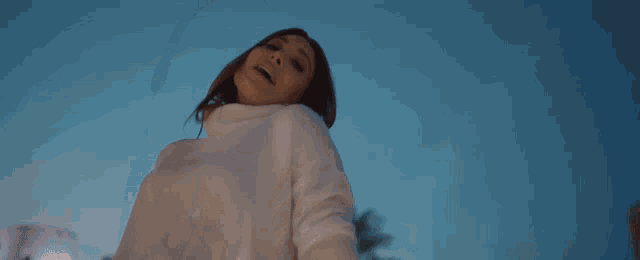 a woman in a white sweater is reaching out her hand towards the sky