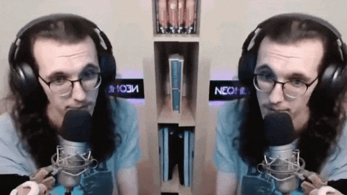 a man wearing glasses and headphones is talking into a microphone with a neon sign behind him