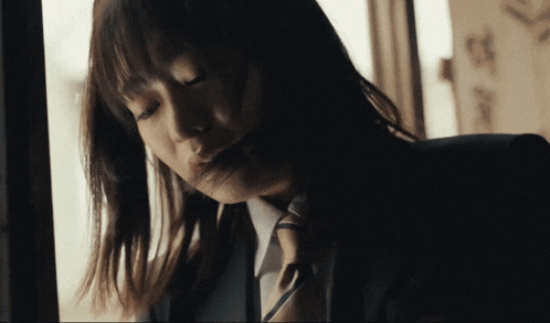 a woman in a suit and tie is looking out of a window