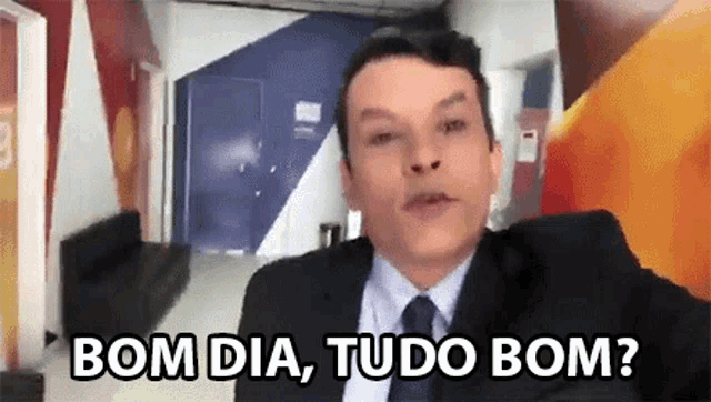 a man in a suit and tie is standing in a hallway and says bom dia tudo bom ?
