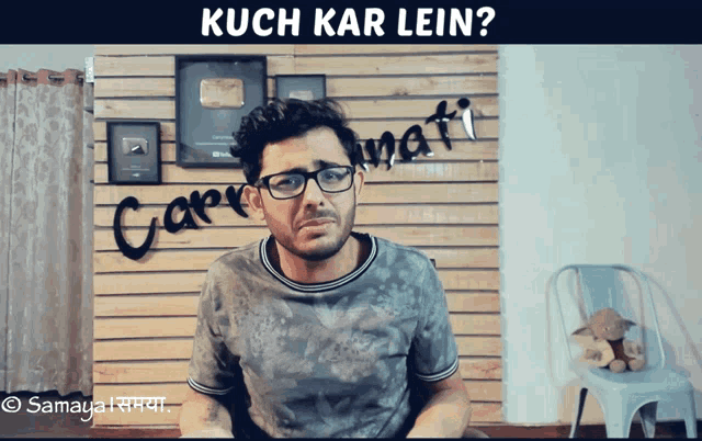 a man wearing glasses is sitting in front of a wooden wall with the words kuch kar lein written on it